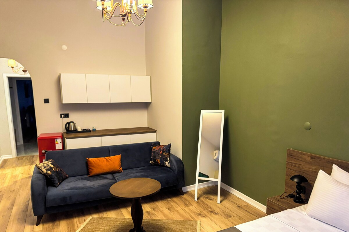Een moderne woonkamer met een bank, een klein rond tafeltje, een bed en een spiegel.
