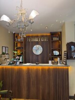 Un mostrador de recepción con una araña, un reloj y un letrero que dice 'FETHI BEY OTEL'.