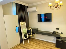 Habitación de hotel con televisión de pantalla plana mostrando 'NETFLIX', un escritorio con una silla, un armario y un equipo de aire acondicionado.