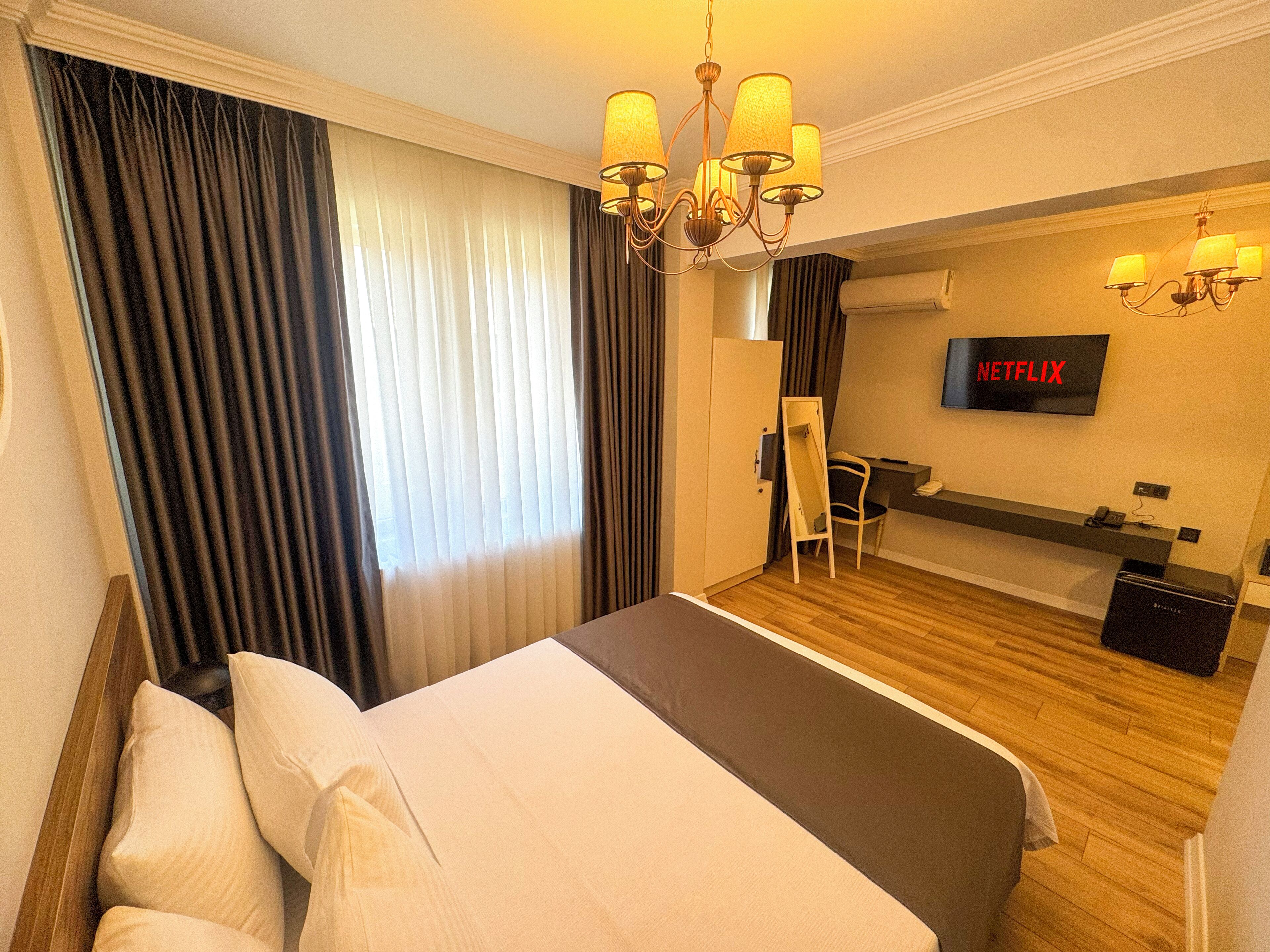 Une chambre d’hôtel comprenant un lit, des rideaux, un bureau avec une chaise, une télévision et un minibar.