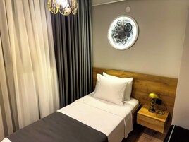 Habitación de hotel con cama, mesita de noche, lámpara, luz circular en la pared y ventana con cortinas.