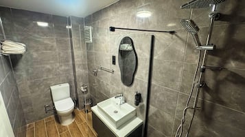 Un baño moderno con inodoro, lavabo, espejo, toallero, ducha y una luz en el techo.