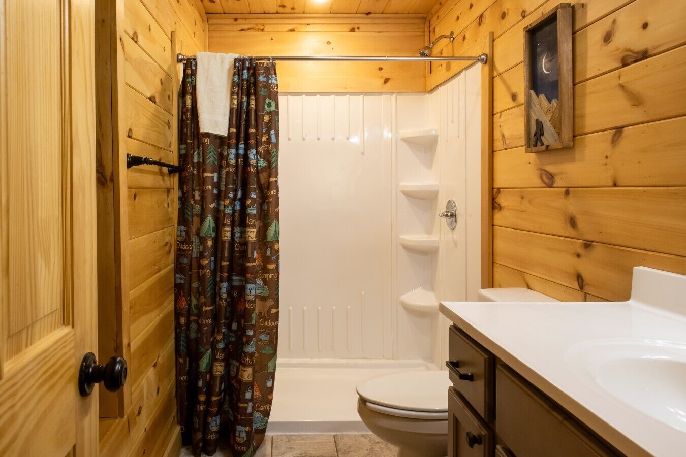 A wooden cabin bathroom with a shower, toilet, and sink.