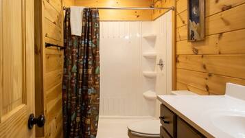 A wooden cabin bathroom with a shower, toilet, and sink.
