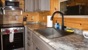 Una cocina con estufa de acero inoxidable, microondas, fregadero y alacenas de madera.