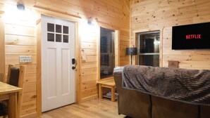 Un interior de madera con una puerta, un banco, un sofá y un televisor de pared mostrando el logotipo de Netflix.