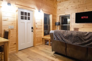 Un interior de madera con una puerta, un banco, un sofá y un televisor de pared mostrando el logotipo de Netflix.