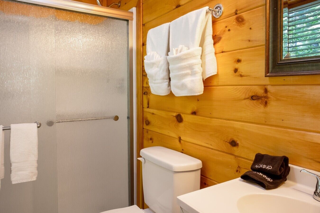 A bathroom with a wooden wall, a toilet, a sink, and a shower door.