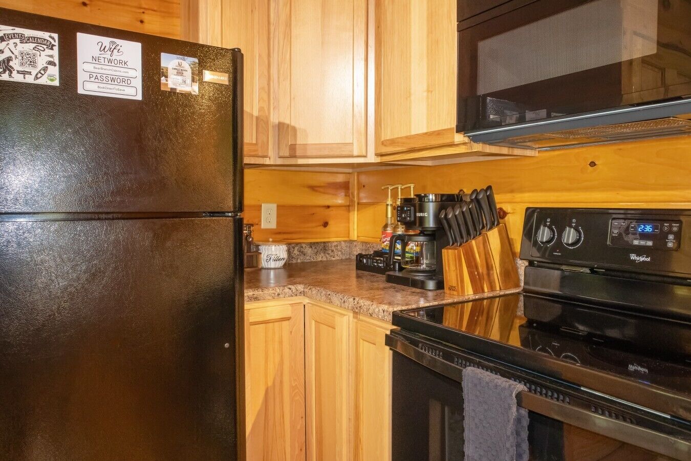 A kitchen with a black refrigerator, wooden cabinets, a coffee maker, and a microwave.
