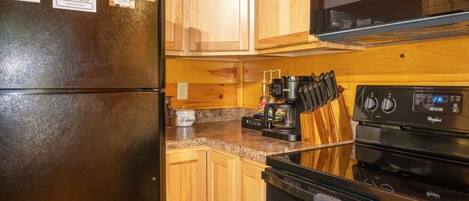 A kitchen with a black refrigerator, wooden cabinets, a coffee maker, and a microwave.