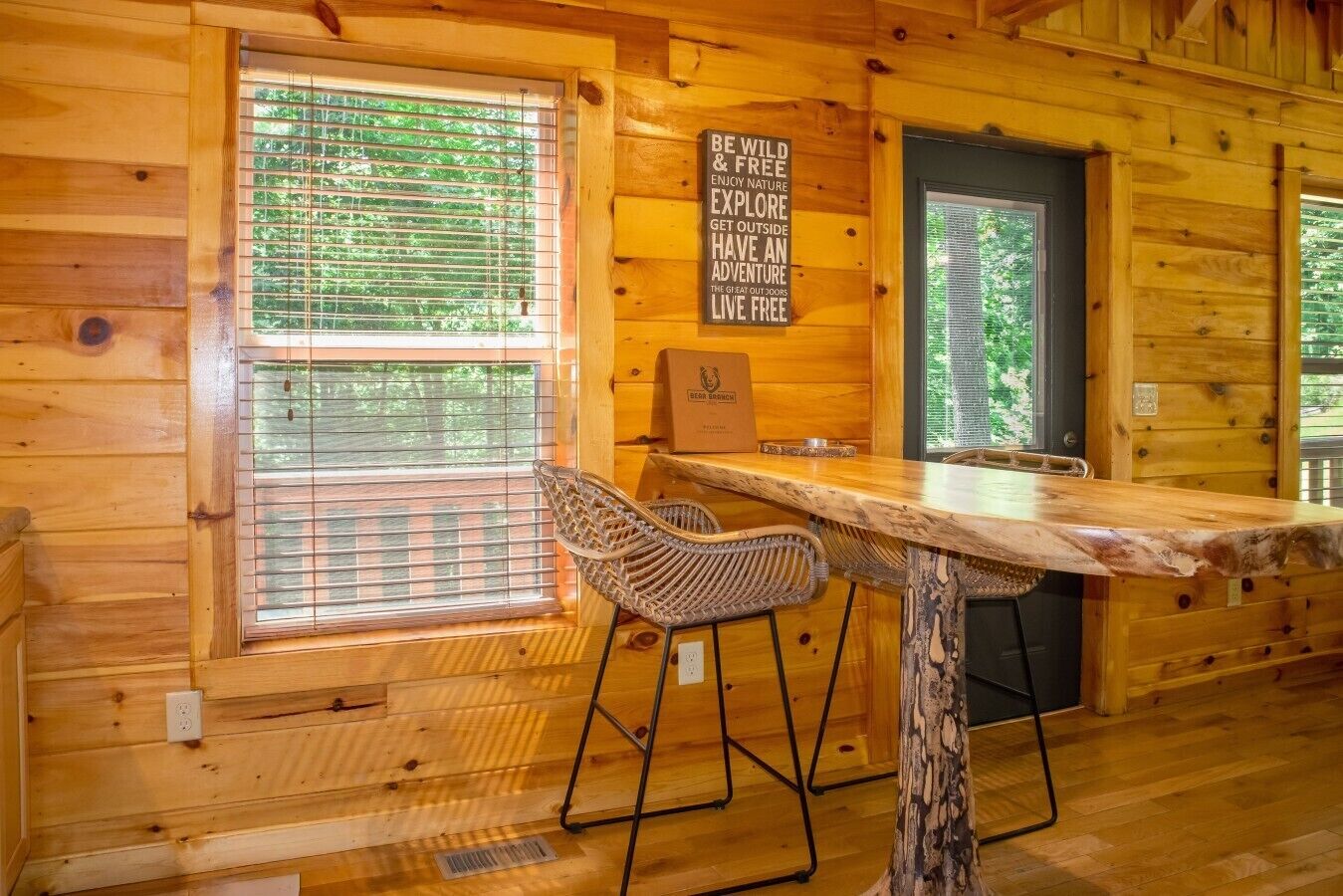 A wooden cabin interior with a bar area, two wicker chairs, a sign encouraging outdoor activities, and a door.