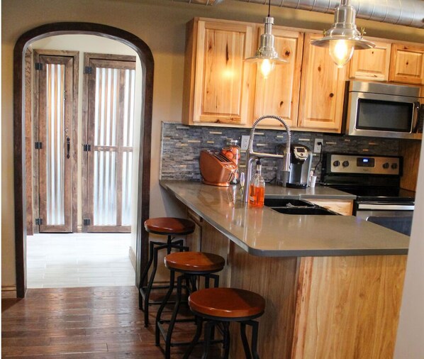 A kitchen with wooden cabinets, a stainless steel microwave, a toaster, and a bar stool. - Buffalo Springs Distilling Company (Stamping Ground)
