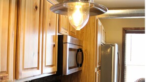 Une cuisine dotée de meubles en bois, d’un réfrigérateur en acier inoxydable, d’un four à micro-ondes et d’un luminaire suspendu.