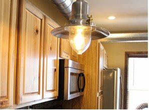 A kitchen with wooden cabinets, a stainless steel refrigerator, a microwave, and a hanging light fixture. - Buffalo Springs Distilling Company (Stamping Ground)