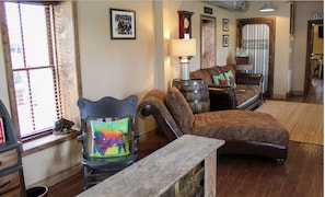 A living room with a wooden floor, a sofa, a chair, a lamp, and a window with blinds. - Buffalo Springs Distilling Company (Stamping Ground)