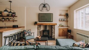 Ein gemütliches Wohnzimmer mit Kamin, einem darüber montierten Fernseher und einer Küchenzeile mit Barhocker.