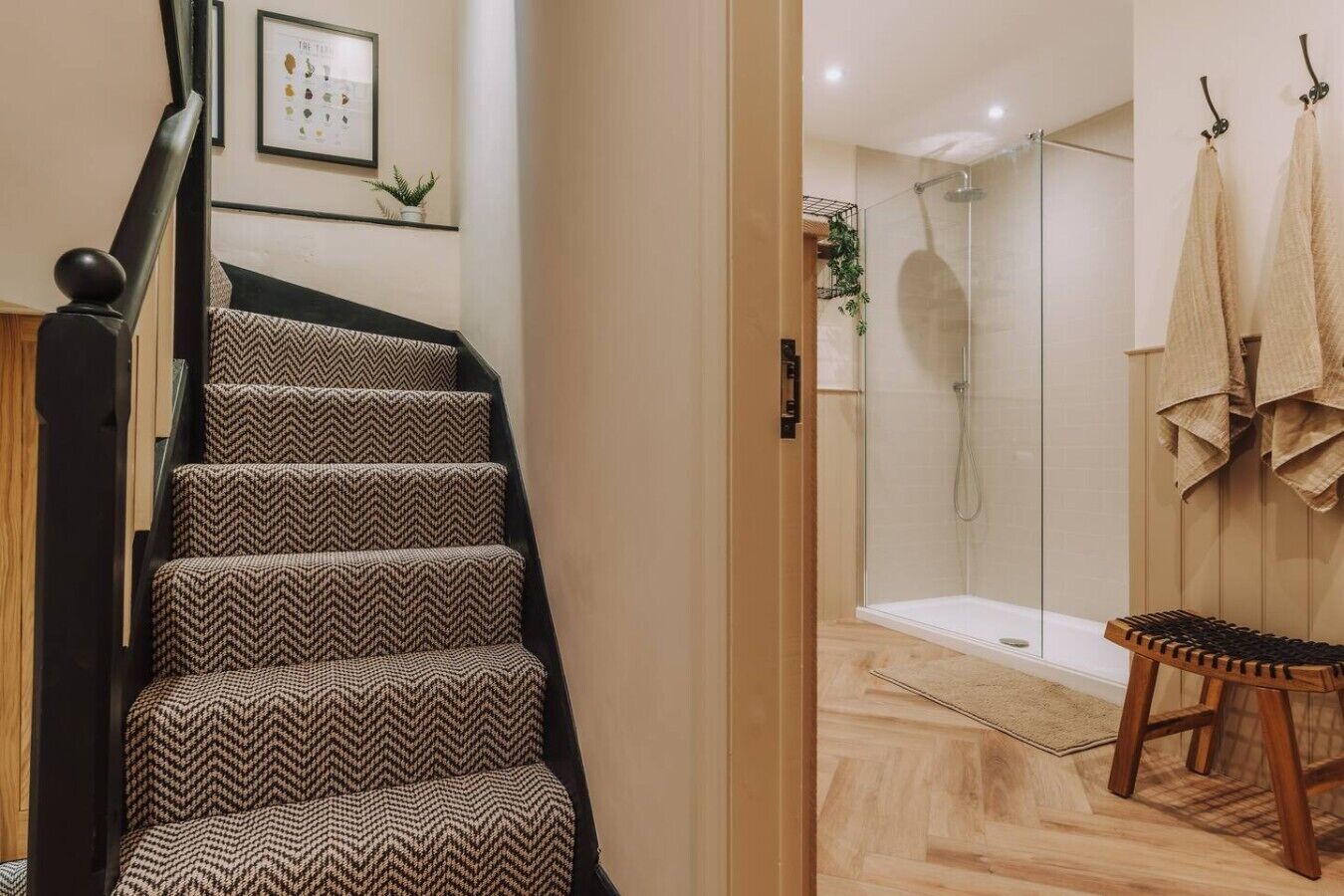 Una escalera con alfombra estampada, una zona de ducha con puertas de vidrio y un banco de madera.