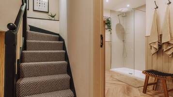 Una escalera con alfombra estampada, una zona de ducha con puertas de vidrio y un banco de madera.