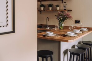 A kitchen with a wooden island, white bowls, wine glasses, and black stools. - The Warren, Stylish Retreat, Bowness on Windermere (Bowness-on-Windermere)