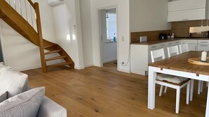 Moderni keittiö, jossa on valkoiset kaapit, puinen ruokapöytä ja portaat.