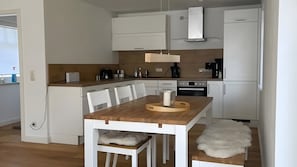 A modern kitchen with white cabinetry, a wooden dining table, and a white furry rug.