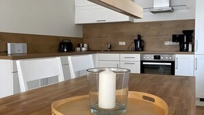 Moderni keittiö, jossa on valkoiset kaapit, puinen työtaso, kahvinkeitin ja lasinen kynttilänjalka puisen tarjottimen päällä.