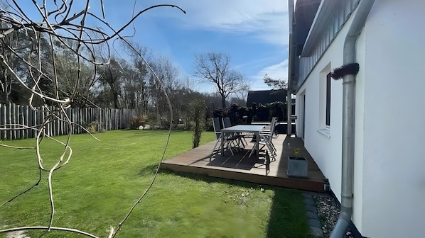 A backyard with a wooden deck, a table with chairs, and a white wall.