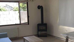 A room with a sofa, a small table, a black heater, and a window with a view of greenery. - House with pool ribadavia (Francelos)