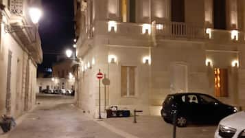 Nachtsicht auf eine Straße mit einem Gebäude, das Balkone und ein parkendes Auto zeigt.