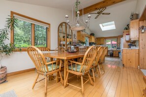 Une table Ă manger en bois, des chaises, un lustre et une vue sur lâextĂ©rieur.