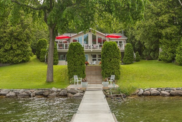 Une propriĂ©tĂ© au bord du lac, dotĂ©e dâun quai menant Ă un bĂątiment avec balcon, le tout entourĂ© dâune vĂ©gĂ©tation luxuriante.