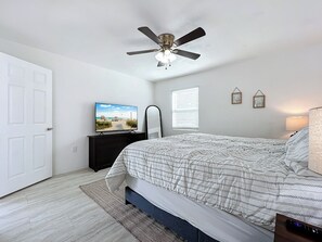 A bedroom with a bed, a ceiling fan, a TV on a dresser, a window with blinds, and a door. - Alta Vida, Cozy Duplex Retreat (Sarasota)