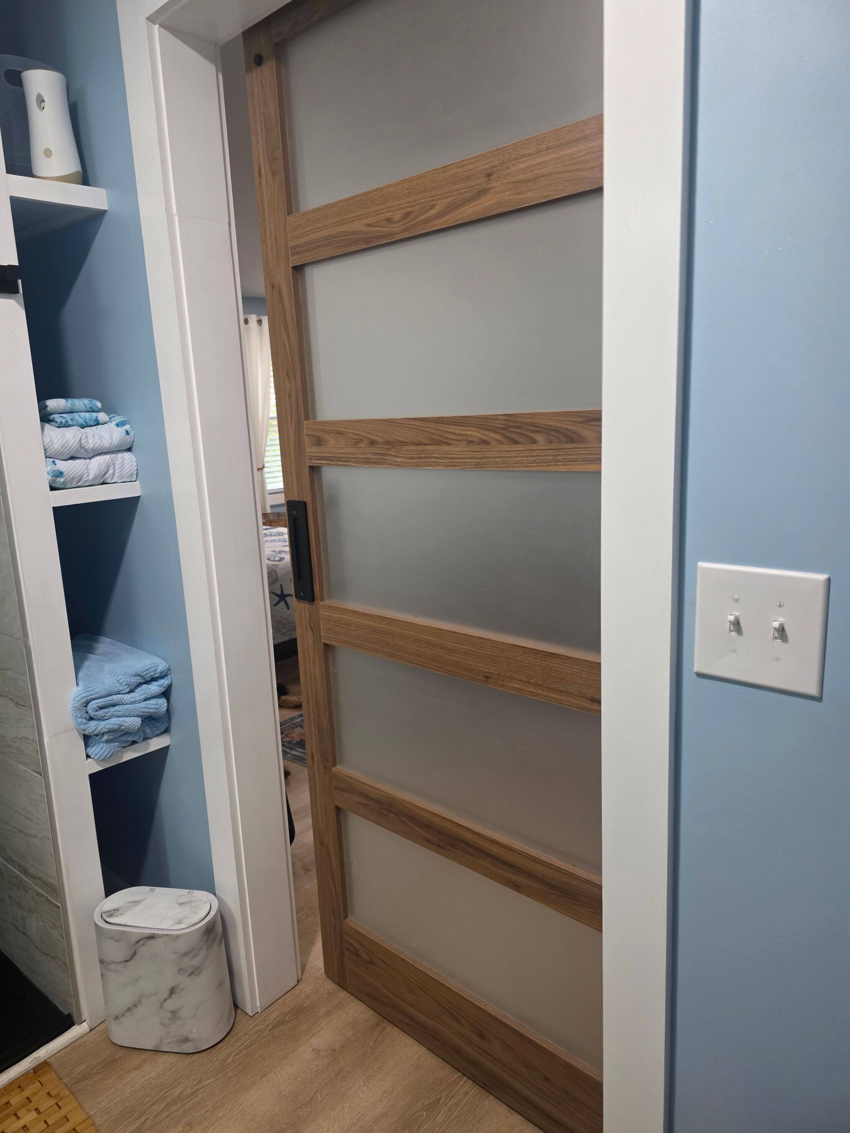Een kamer met een schuifdeur, een marmeren vloer, een witte muur en een plank met opgevouwen handdoeken.