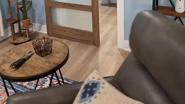 Een kamer met een schuifdeur in boerderijstijl, een klein rond tafeltje met een afstandsbediening, een kamerkleed met een patroon en een bank.