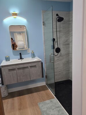 A bathroom with a glass shower enclosure, a vanity with a mirror, and a light fixture above the mirror. - Modern Guesthouse Near Beaches & FLETC (Brunswick)