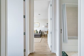 Ein Flur, der in ein Wohnzimmer mit Sofa, Lampe und Blickrichtung zu einem Badezimmer mit Dusche führt.
