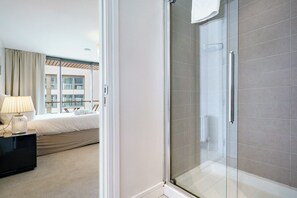 Ein Hotelzimmer mit einem Bett, einer Nachttischlampe, einer Duschkabine und Blick auf ein Gebäude.
