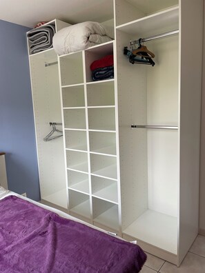 A bedroom with a bed, a purple blanket, a white wardrobe with multiple shelves, and a red item on top. - Apartment 10 min Montpellier and 10 min beaches (Lattes)