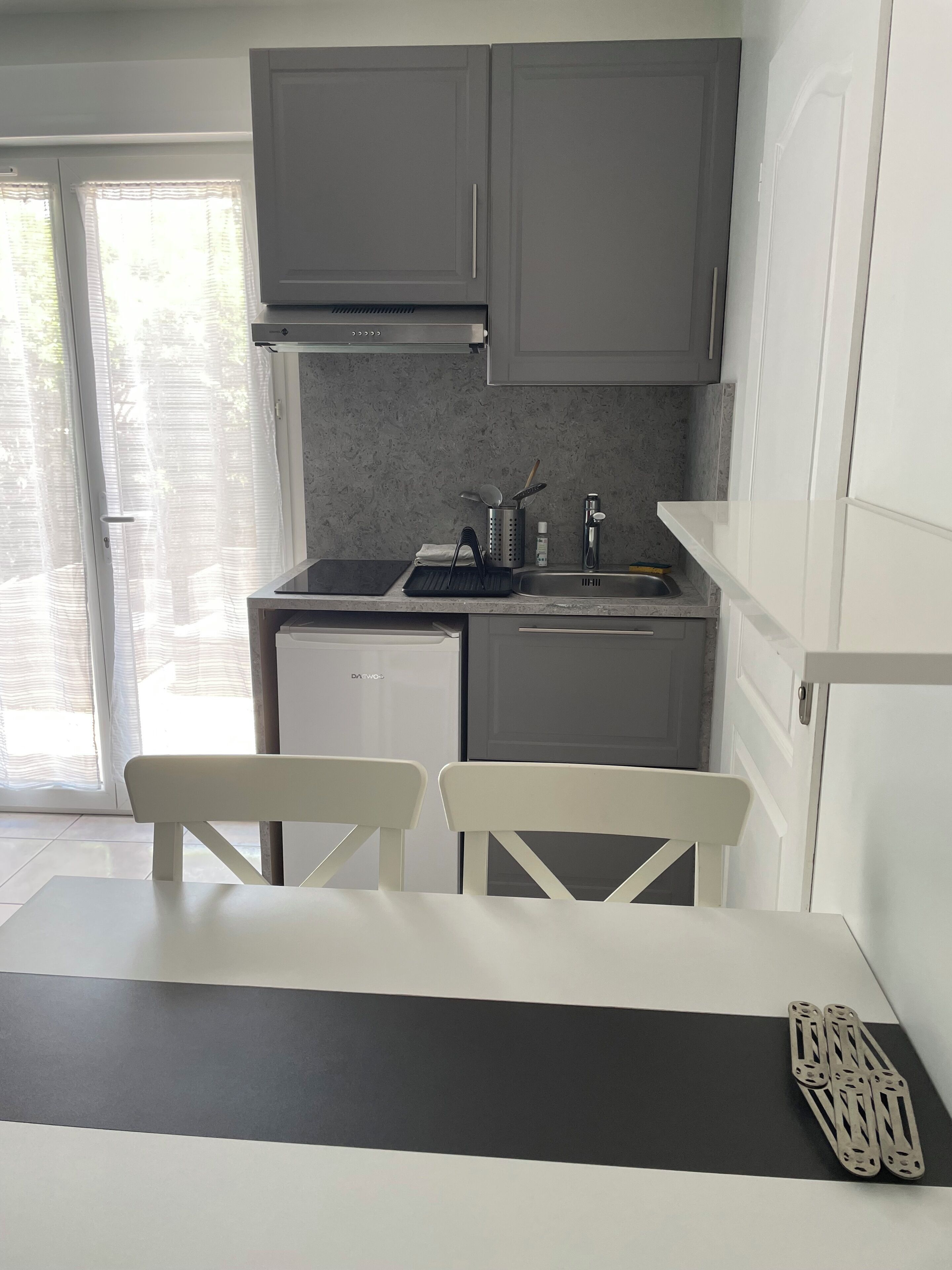 A compact kitchen with grey cabinets, a small dishwasher, and a dining area with two white chairs.