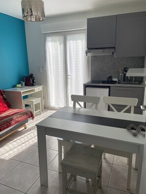 A modern kitchen with grey cabinets, a white countertop, and a built-in oven. There is a dining table with chairs and a small white stool. - Apartment 10 min Montpellier and 10 min beaches (Lattes)