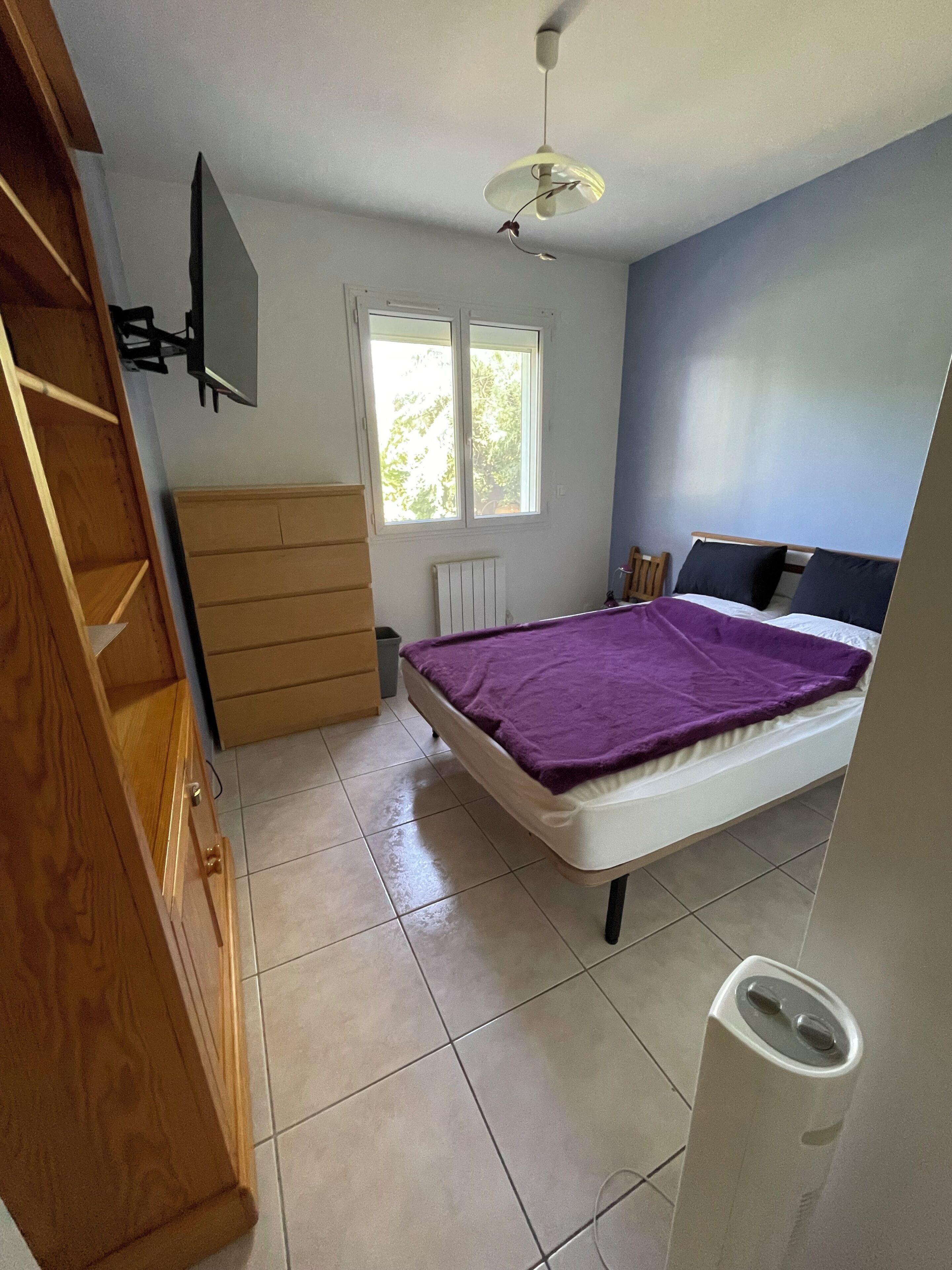 Un dormitorio con cama, ventana, ventilador de techo y armario de madera.