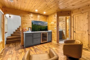 Ein Holzinnenraum mit Küchenzeile, einem an der Wand befestigten Fernseher und einer Treppe, die eine weitere Ebene hinaufführt.