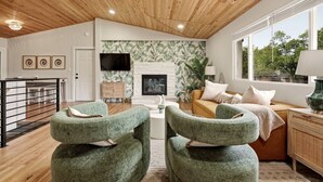 Ein Wohnzimmer mit Kamin, grünen Sesseln, einer Couch und einem Fernseher.