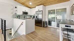 Eine moderne Küche mit weißen Schränken, einem Edelstahlkühlschrank und einer Holzzieldecke.