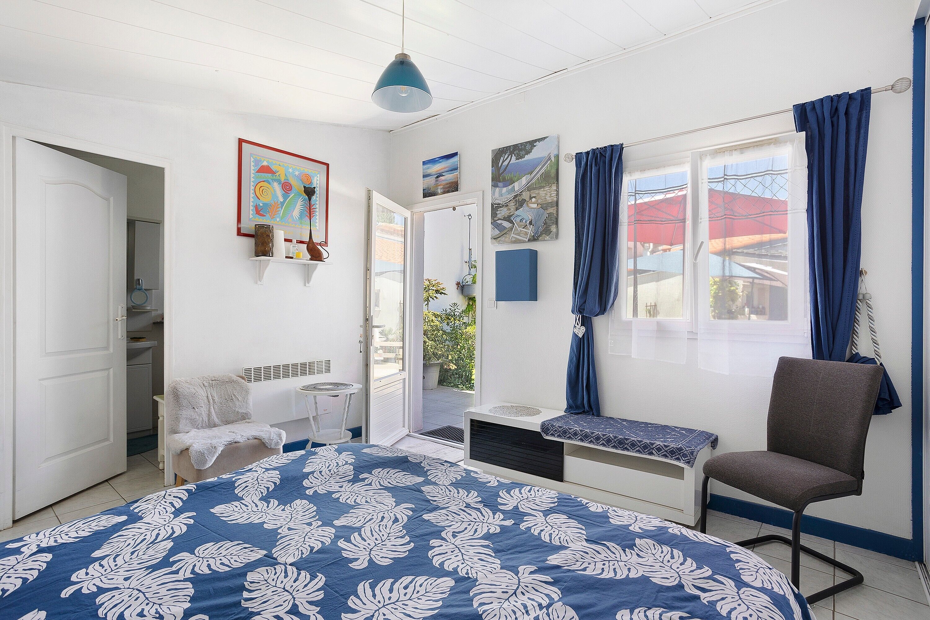 A bedroom with a bed, a chair, a window with curtains, and a door leading to another room.