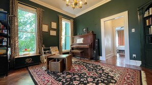 A room with a piano, a bookshelf, a desk, a rug, and a window with curtains. - Charming, Spacious Victorian Near Downtown Dallas (Dallas)