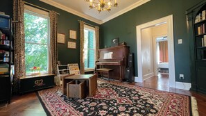 A room with a piano, a bookshelf, a desk, a rug, and a window with curtains. - Charming, Spacious Victorian Near Downtown Dallas (Dallas)