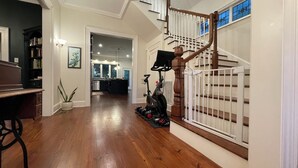 A spacious hallway with hardwood floors, a staircase with a wooden railing, and a view into the kitchen area. - Charming, Spacious Victorian Near Downtown Dallas (Dallas)