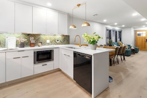 A modern kitchen with white cabinets, a dishwasher, and a dining area with chairs and a table. - North End 2BR Home / Prime Boston Location (Boston)