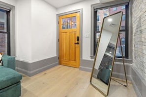 A room with a wooden door, a large mirror, and a view of buildings through a window. - North End 2BR Home / Prime Boston Location (Boston)